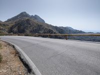 a large motorcycle is riding down an empty road over a mountain side, near the water