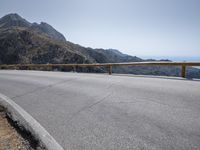 a large motorcycle is riding down an empty road over a mountain side, near the water