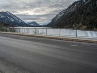 two motorcycles on a long paved highway near a large mountain lake surrounded by snow capped trees