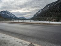 two motorcycles on a long paved highway near a large mountain lake surrounded by snow capped trees