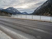 two motorcycles on a long paved highway near a large mountain lake surrounded by snow capped trees