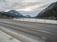 two motorcycles on a long paved highway near a large mountain lake surrounded by snow capped trees