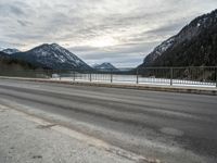 two motorcycles on a long paved highway near a large mountain lake surrounded by snow capped trees