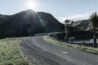 there is a truck that is driving on a road near some mountains and trees with the sun in the background