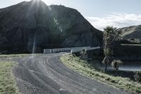 there is a truck that is driving on a road near some mountains and trees with the sun in the background