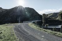 there is a truck that is driving on a road near some mountains and trees with the sun in the background