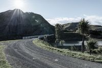 there is a truck that is driving on a road near some mountains and trees with the sun in the background