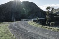 there is a truck that is driving on a road near some mountains and trees with the sun in the background