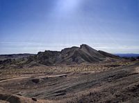 a dirt hill with some large rocks and dirt road passing by it on a sunny day