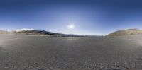 panoramic shot of a road with no traffic visible in it with sun and mountain range