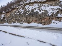 a snow bank along the side of a mountain road near mountains with rocks and snow