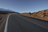 there is an empty mountain road winding towards a snowy mountain range on the horizon,