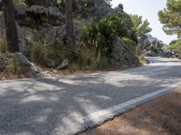 a black motorcycle is stopped on the side of a mountain road and is surrounded by rocks