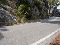 a black motorcycle is stopped on the side of a mountain road and is surrounded by rocks