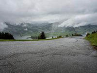 the landscape is covered with many different views and clouds, and a winding road leads towards some mountains and a small lake