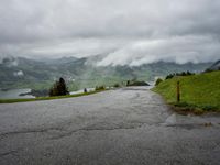 the landscape is covered with many different views and clouds, and a winding road leads towards some mountains and a small lake