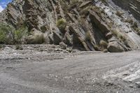 a motorcycle parked in front of some rocks and bushes on a mountain road between mountains