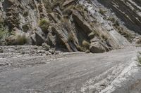 a motorcycle parked in front of some rocks and bushes on a mountain road between mountains