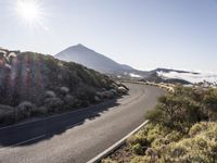 a road running up the side of a mountain near the ocean with sun going through the clouds