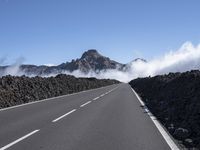 a road is surrounded by mountains and fog in the distance on a sunny day with only a few clouds to be seen