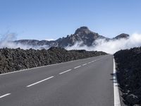 a road is surrounded by mountains and fog in the distance on a sunny day with only a few clouds to be seen