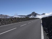 a road is surrounded by mountains and fog in the distance on a sunny day with only a few clouds to be seen