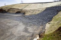 a steep mountain of gravel and some dirt is shown to the left of the road