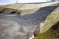 a steep mountain of gravel and some dirt is shown to the left of the road