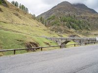 the motorcycle is traveling on a mountain road near a fence and stone bridge over a valley