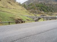 the motorcycle is traveling on a mountain road near a fence and stone bridge over a valley