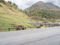 the motorcycle is traveling on a mountain road near a fence and stone bridge over a valley