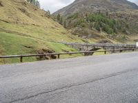 the motorcycle is traveling on a mountain road near a fence and stone bridge over a valley