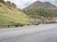 the motorcycle is traveling on a mountain road near a fence and stone bridge over a valley