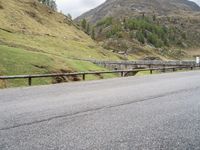 the motorcycle is traveling on a mountain road near a fence and stone bridge over a valley