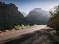 a person riding a bike down a mountain road in the desert area in front of rocks and trees