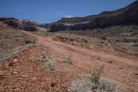 an empty dirt road in the mountains near some rocks and trees in the distance is a canyon