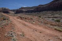 an empty dirt road in the mountains near some rocks and trees in the distance is a canyon