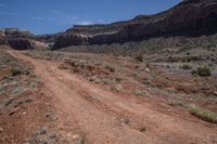 an empty dirt road in the mountains near some rocks and trees in the distance is a canyon