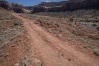 an empty dirt road in the mountains near some rocks and trees in the distance is a canyon