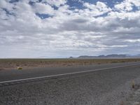 an empty paved road in the middle of a desert plain under a blue sky with white clouds