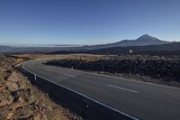 a lone car drives down an empty desert road near a volcano on a mountaintop