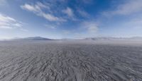 a vast view of a mountain and sand plain and mountains with blue skies above them