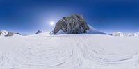 a mountain with snowboarders in the foreground and a sun shine over it