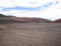 the sky above the mountains shows red rocks, clouds and a lone orange rock that lies flat