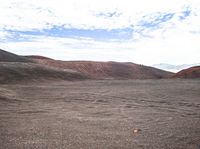 the sky above the mountains shows red rocks, clouds and a lone orange rock that lies flat