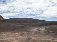 some dirt hills with hills in the background with clouds in the sky and a person on a skateboard