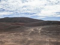 some dirt hills with hills in the background with clouds in the sky and a person on a skateboard