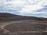 some dirt hills with hills in the background with clouds in the sky and a person on a skateboard