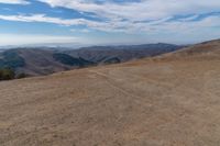 there is a bench on a hill near the mountains with a view of the hills in the back