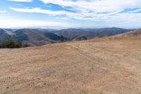 there is a bench on a hill near the mountains with a view of the hills in the back